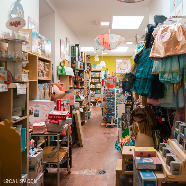 Allée centrale du magasin de jouets Le Pont des Arts à Huy, avec des jouets et des déguisements.