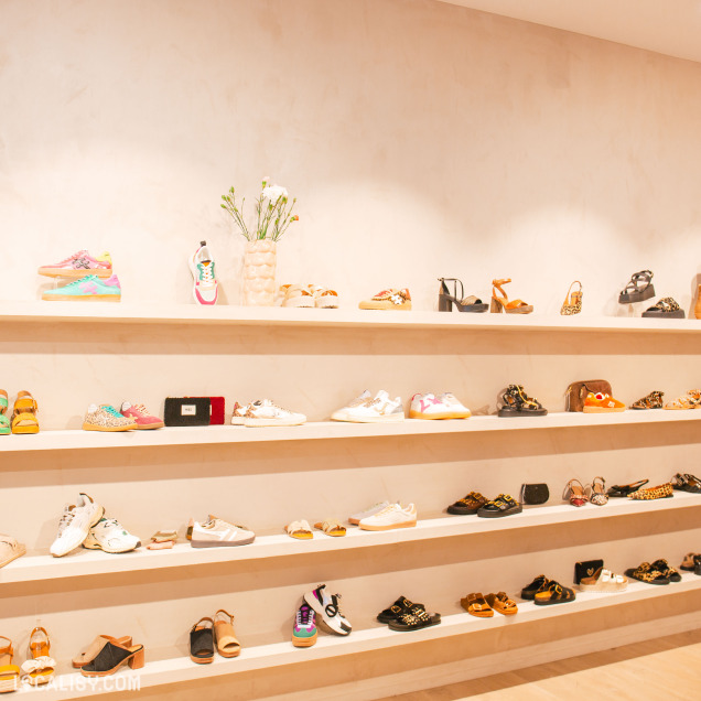 Présentation de chaussures à talons hauts et de sandales colorées sur des étagères au magasin Factory Store à Liège.