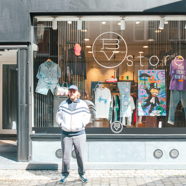 Façade extérieure du magasin de streetwear BV Store à Liège avec sa vitrine et une personne posant devant.