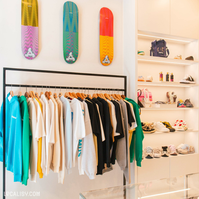 Intérieur du magasin streetwear BV Store à Liège, présentant des vêtements sur cintres et des baskets sur étagères éclairées.