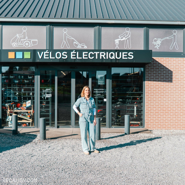 Façade extérieure du magasin de vélos électriques E-bike à Nandrin, avec l'enseigne "VÉLOS ÉLECTRIQUES" et une personne posant devant.