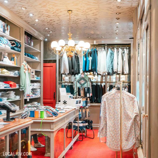 Intérieur du magasin de vêtements pour hommes Boutique Mainfroid à Huy, avec le comptoir et des chemises exposées.