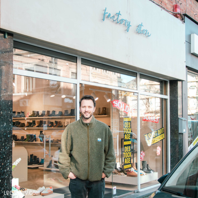 Façade du magasin de chaussures Factory Store à Huy, avec un homme posant devant la vitrine.
