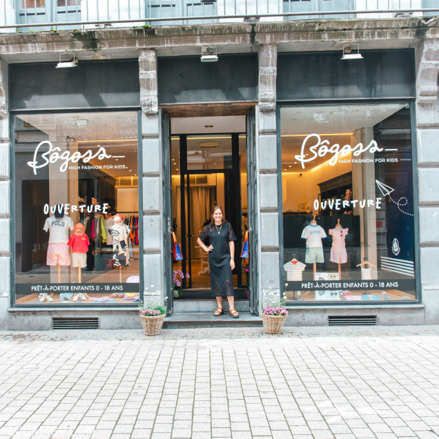 Façade extérieure de la boutique de vêtements pour enfants Bogoss Boutique à Liège, avec l'enseigne et une personne posant devant la porte.
