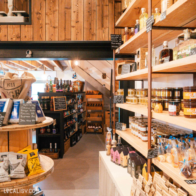 Une épicerie chaleureuse à l’ambiance rustique expose soigneusement des produits locaux artisanaux sur des étagères en bois.