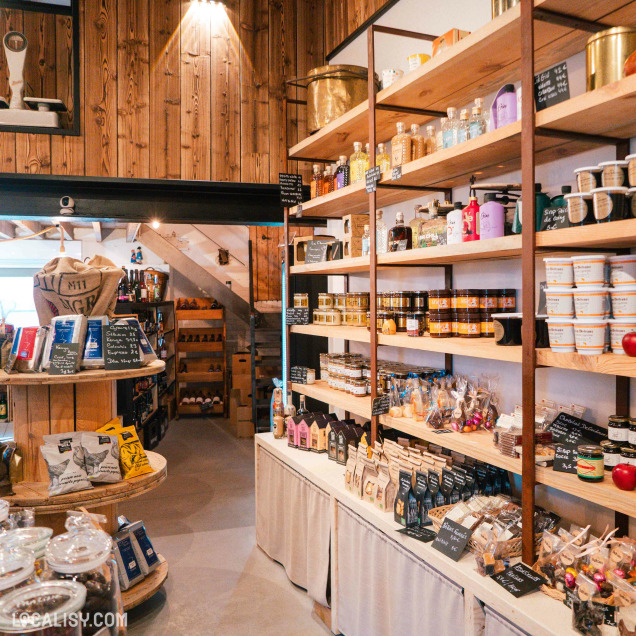 Une jolie épicerie chaleureuse et artisanale, aux étagères remplies de produits locaux soigneusement présentés dans un décor bois naturel.