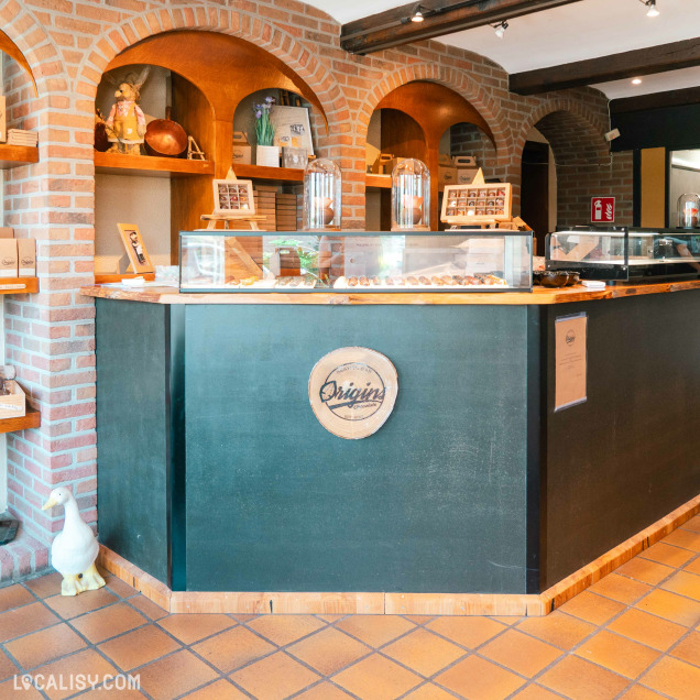 L’intérieur chaleureux de la chocolaterie Origins allie charme rustique et présentation soignée, mettant en valeur des créations artisanales derrière un élégant comptoir en bois.