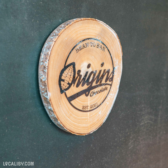 Un logo gravé sur une tranche de bois brut affiche fièrement l’identité artisanale de la chocolaterie Origins, fondée en 2021.