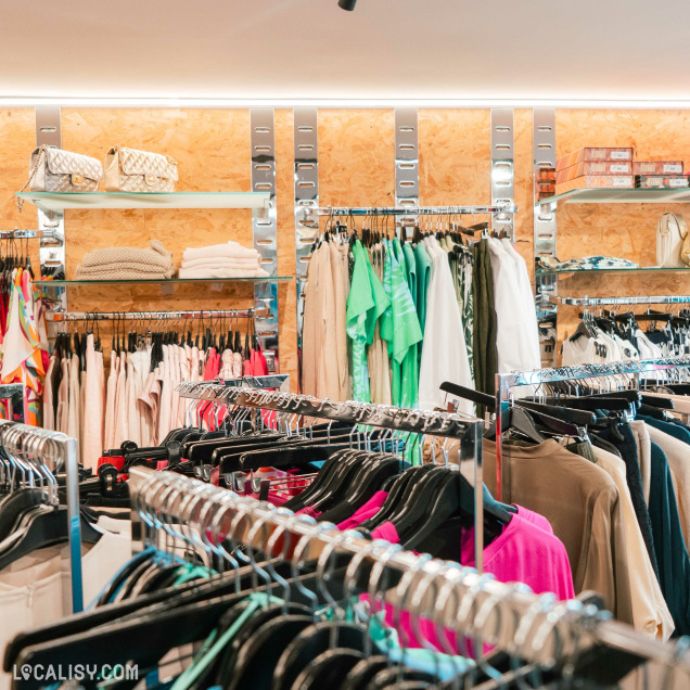 Sélection de sacs à main et de vêtements suspendus sur des portants dans le magasin de mode Autrement Féminin à Nandrin.