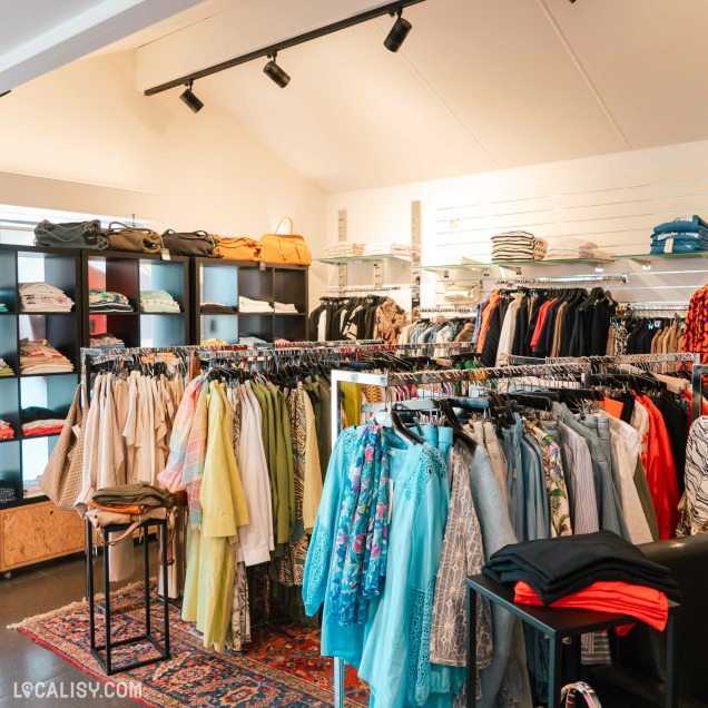 Vue intérieure du magasin de vêtements pour femmes Autrement Féminin à Nandrin, avec une variété de tenues.