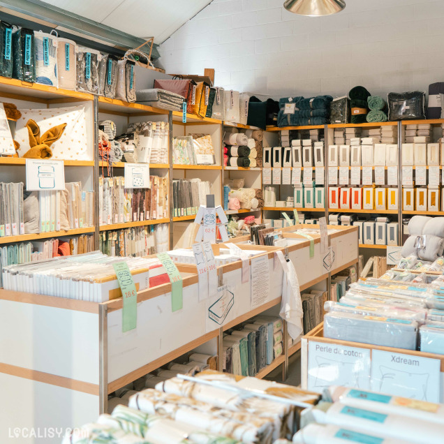 Intérieur d’un magasin de linge de maison avec des étagères remplies de draps, housses et textiles soigneusement rangés et étiquetés.