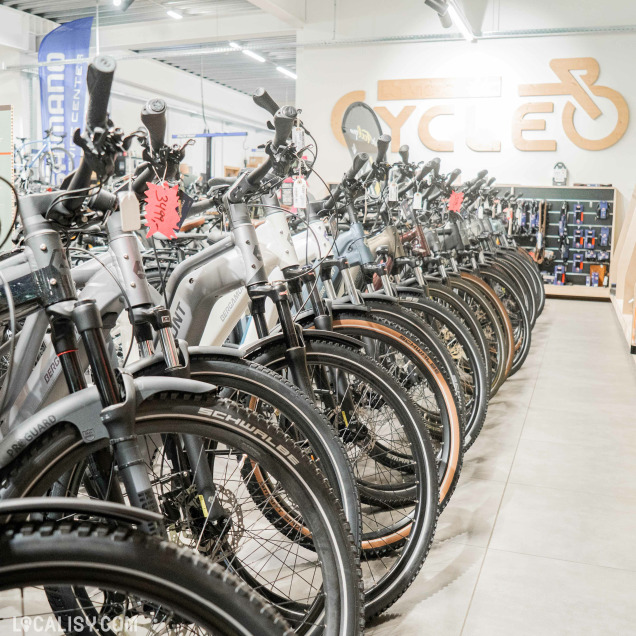 Le comptoir d’accueil du magasin Cycleo est visible avec le logo en bois en arrière-plan et des accessoires de vélo en exposition.